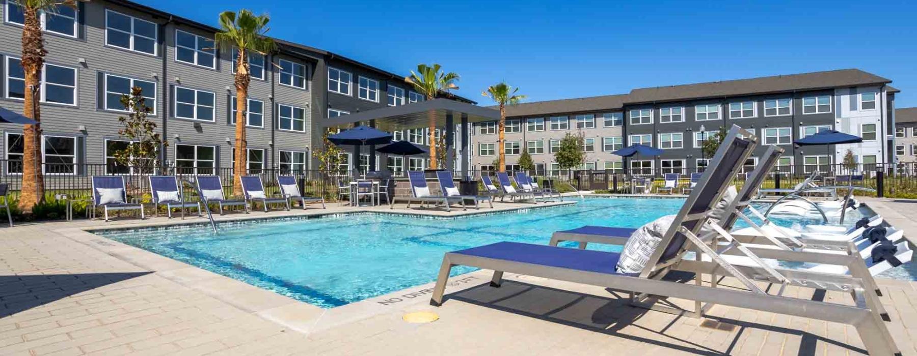 a pool with chairs and umbrellas by a building